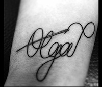 tatuaje en blanco y negro en la pierna: olga escrito como si g¡fuera hilo y una aguja