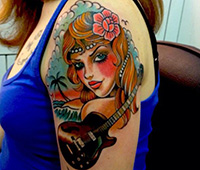 tatuaje en el brazo: chica cn guitarra y playa